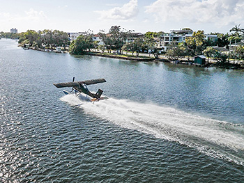 Seaplane landing on Maroochy River with boat houses in the background