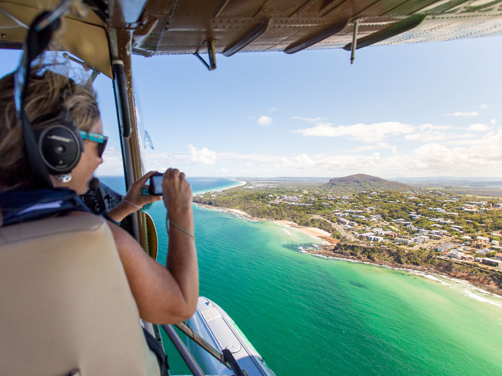 Woman taking photos from seaplane with doors off and panoramic views of sunshine coast at Coolum